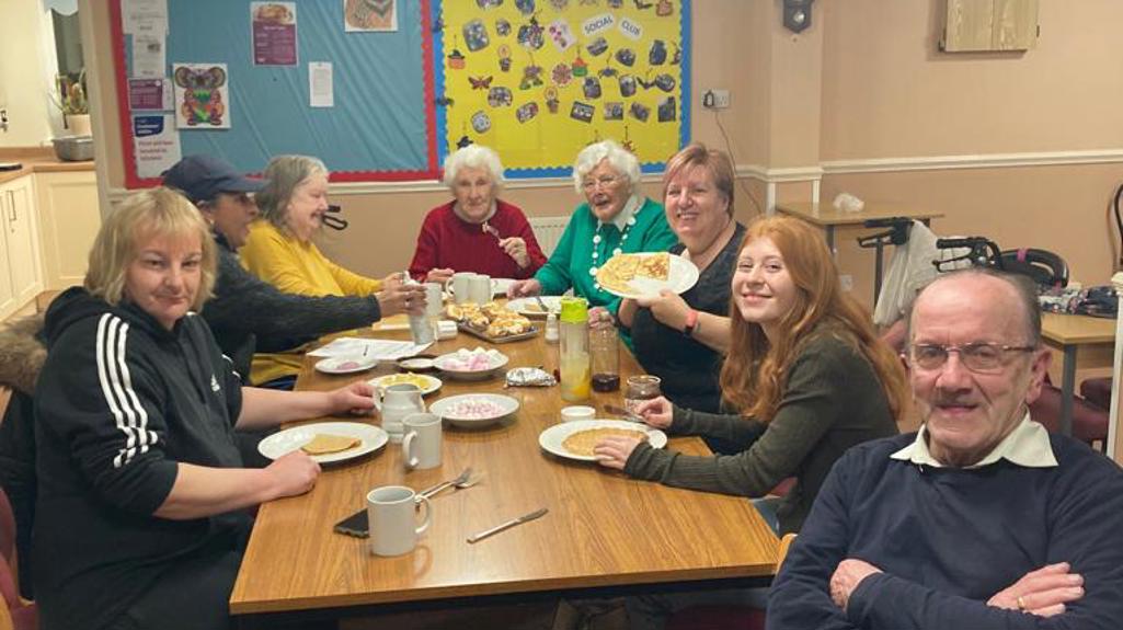 Group of people sitting round a table smiling and holding plates of pancakes