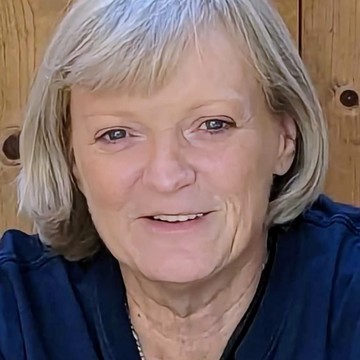 Picture of Carol smiling and wearing a blue top with a silver necklace 