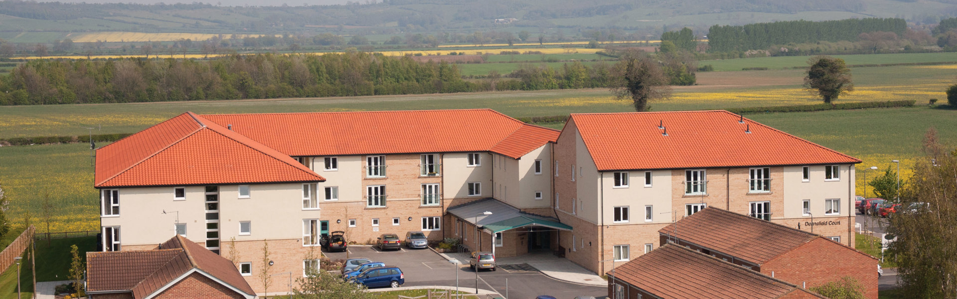 A photograph of a few different houses and a building of flats with fields in the background and a grey sky. 