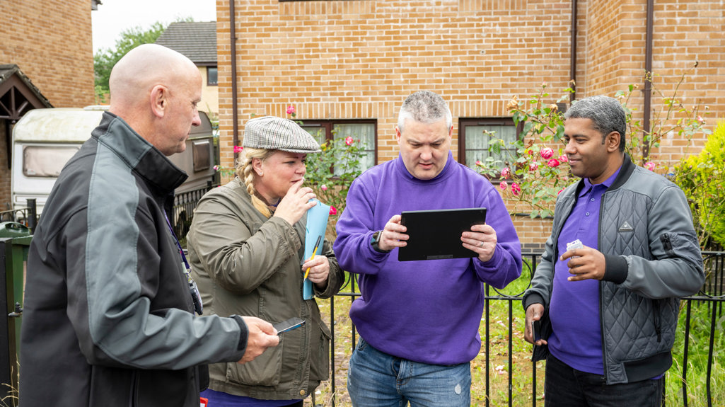 A group of yorkshire housing colleagues standing outside a yorkshire housing home smiling and looking at a tablet. 