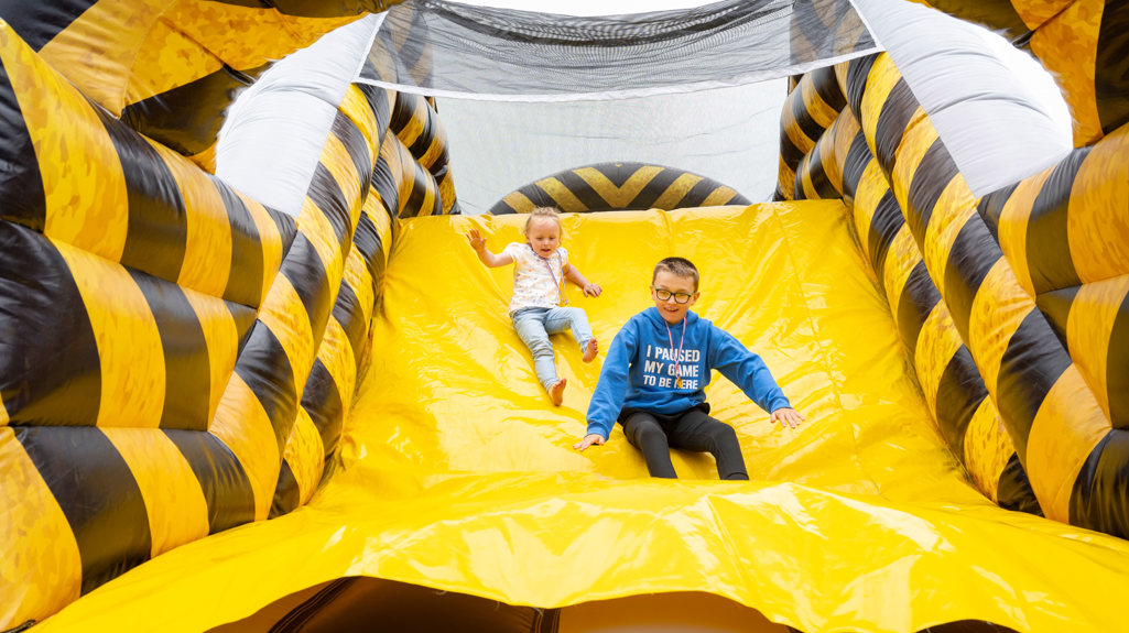 Two children sliding down a giant inflatable slide smiling 