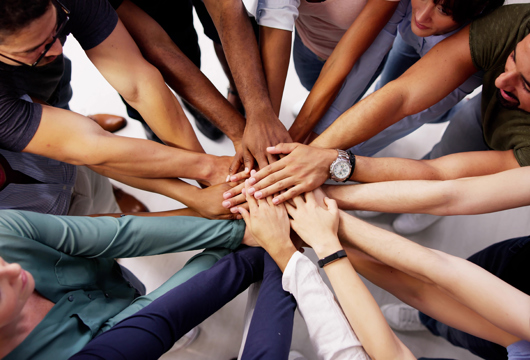 A photograph of multiple people's hands all joined together in the middle of a circle. 