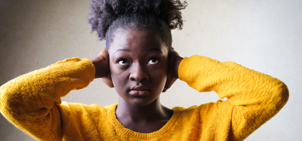 A woman wearing a yellow jumper and holding her hands over her ears. 