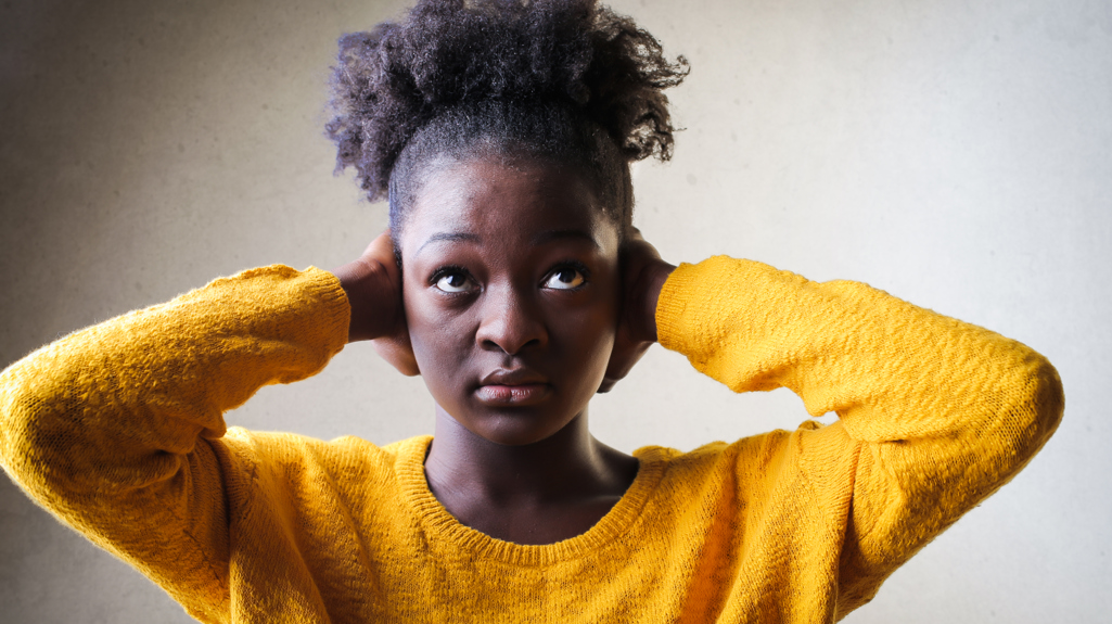 A woman wearing a yellow jumper and holding her hands over her ears. 