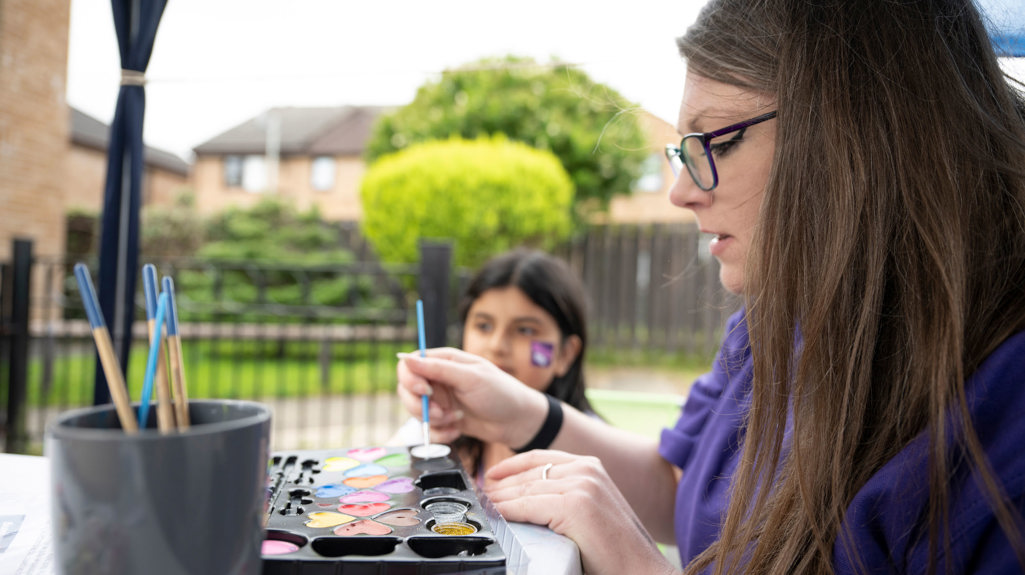 A yorkshire housing colleague and a child at a craft stall doing some painting 