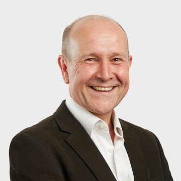 A man smiling at the camera wearing a black blazer and white shirt 