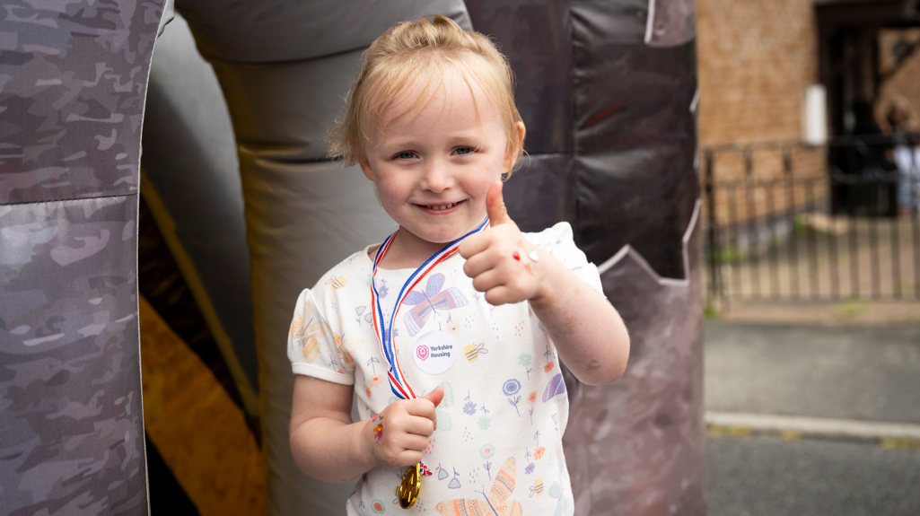 Young girl holding a medal with her thumbs up and smiling at the camera having just completed the obstacle course. 