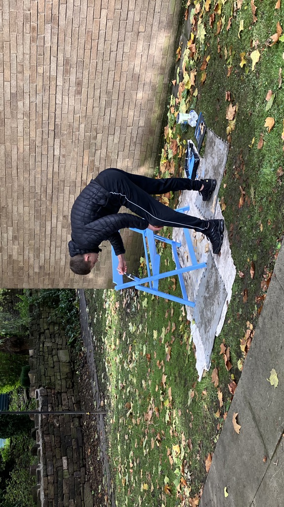 A man painting a blue chair outside on the grass with protective sheets covering the floor