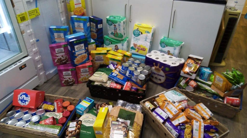 A collection of cereal, toilet roll, biscuits and pasta for a food bank donation in a kitchen. 