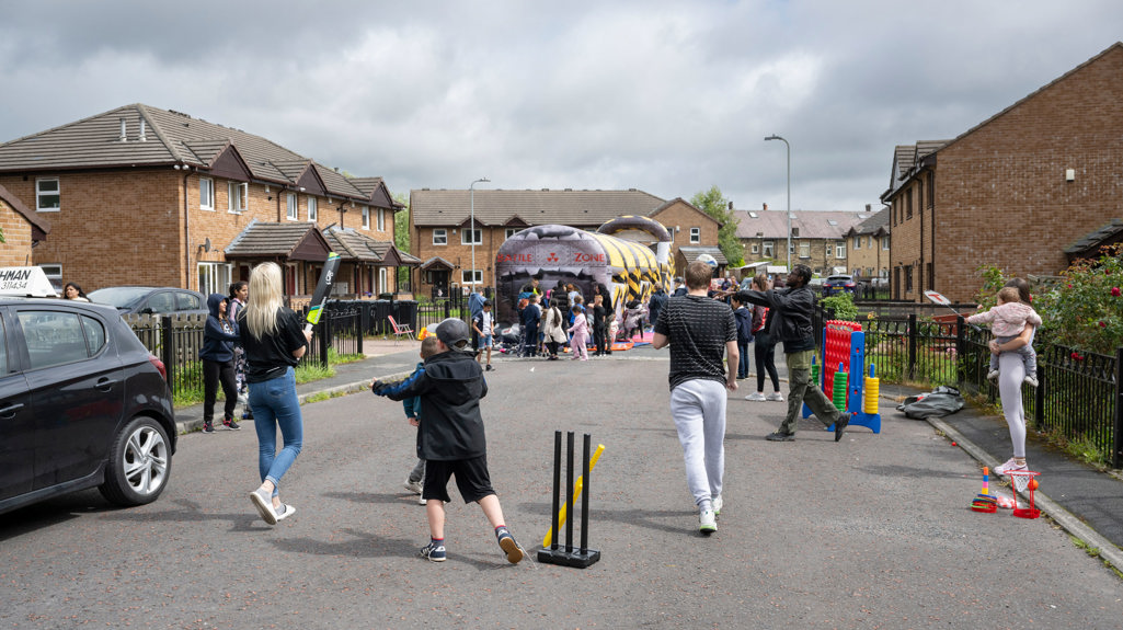 A number of people playing various street games like cricket and an obstacle course 