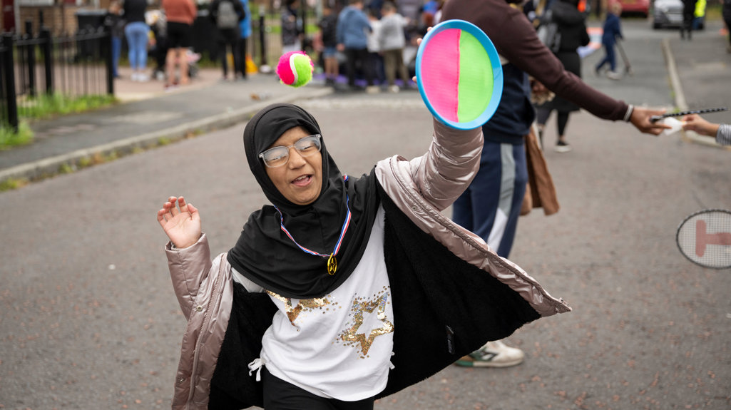 A girl playing in the busy street with a velcro pad and ball 