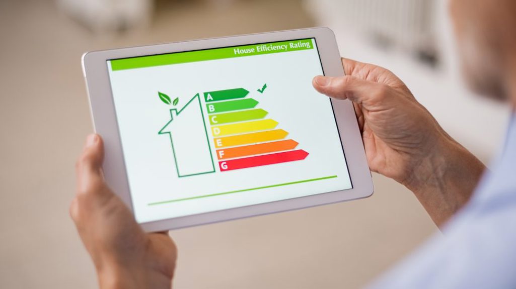 Photograph of hands holding a white iPad-style tablet showing EPC ratings with a tick next to the A rating section. 