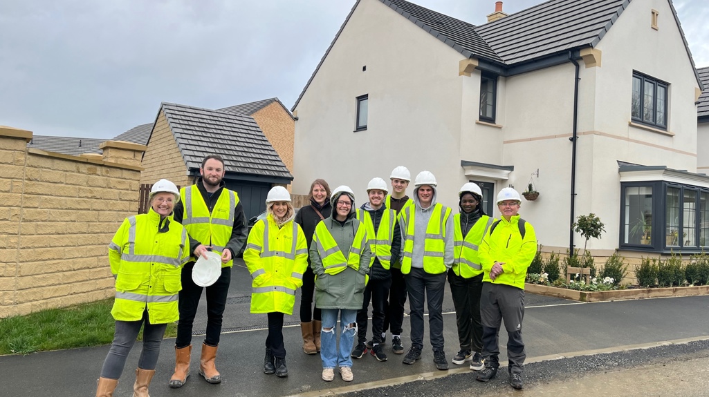 A group of students standing infront of a new build development all wearing high visibility clothing 