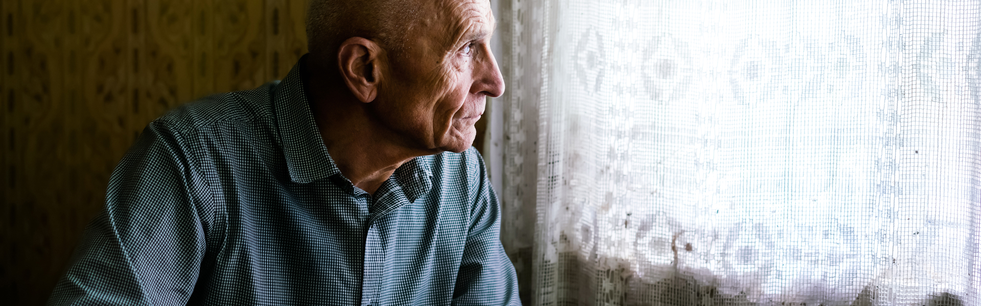 A man looking out the window through a netted curtain. 