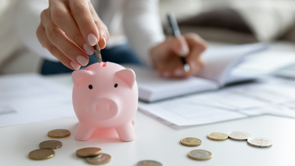 Woman putting coins into a pink piggy bank