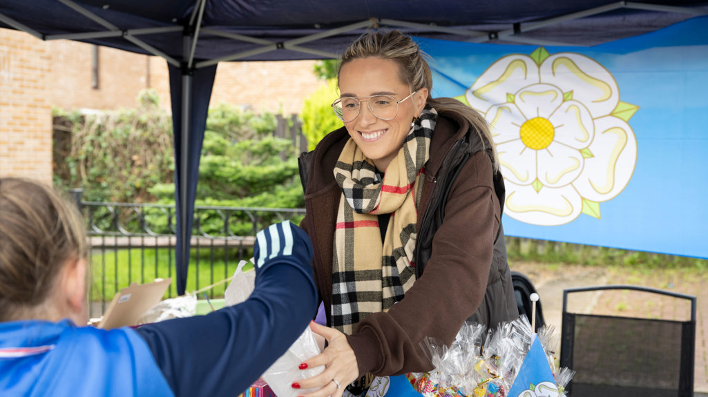 A woman smiling while standing behind a stall handing a child a goody bag