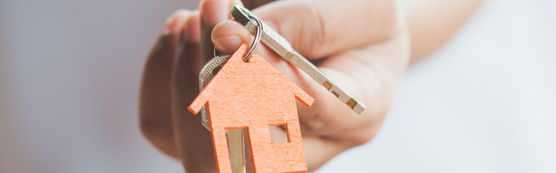 Person in white t-shirt holding out a set of keys with an orange house keyring, in front of them, towards the camera.